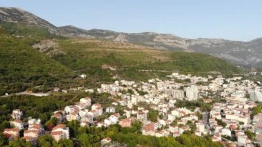 Karadağ 'daki Adriyatik Denizi kıyısındaki Petrovac kasabası. Arka planda dağ manzarası ve marinası olan koyu kırmızı fayanslı evler olan bir kasaba. Yüksek kalite 4k görüntü