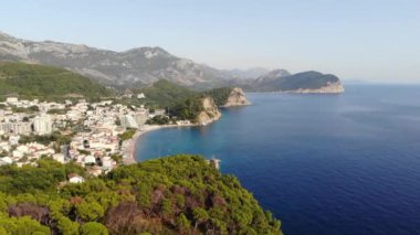 Karadağ 'daki Adriyatik Denizi kıyısındaki Petrovac kasabası. Arka planda dağ manzarası ve marinası olan koyu kırmızı fayanslı evler olan bir kasaba. Yüksek kalite 4k görüntü