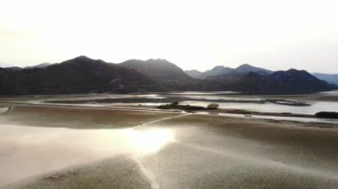 Havadan Skadar Gölü Karadağ 'ı çektiler. Gün batımında dağlarda çimenli bir gölün drone videosu. Dağ manzarası, kayalar, su ve yeşillik. Yüksek kalite 4k görüntü