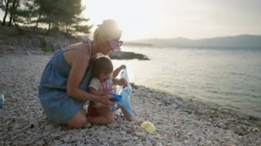 Kız plajdaki deniz kenarındaki çöpe plastik atıyor. Aile doğayı temizler ve çevreyi korur..