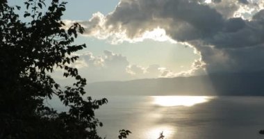 Ohri Gölü Makedonya. Dağların arasında duran göl manzarası. Güneşin içinden geçtiği desenli bulutlarla dolu güzel bir gökyüzü. Işınlarını görebilirsiniz. Yüksek kalite 4k görüntü