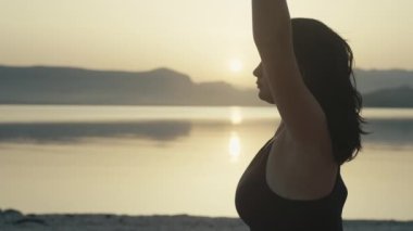 Deniz kenarında güneş üzerine meditasyon yapan bir kızın yakın çekimi. Sahilde yoga yapan bir kadın güzel bir okyanus manzarası, aktif bir yaşam tarzı. Yüksek kalite 4k görüntü