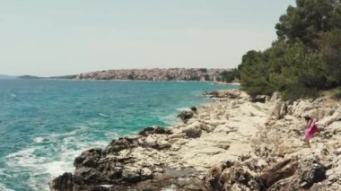Hava manzarası okyanus kıyısındaki kayalıklara gider. Yaz tatilinde, güzel bir manzarada, deniz kenarında güneşlenen bir kadın..