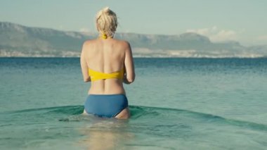 Slow motion video of an older woman entering the ocean and diving into the water. Beautiful European woman swims in the sea on summer vacation.
