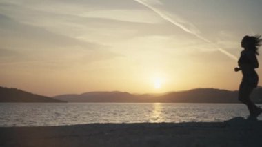 Gün batımında deniz kenarında koşan bir kızın hızlandırılmış videosu. Güzel okyanus manzarasında gün doğumunda aktif yaşam tarzı egzersizi. Yüksek kalite 4k görüntü
