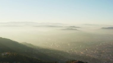 Aerial view Sarajevo Bosnia and Herzegovina. Drone flying in the west, sunrise over the city with houses, streets that are covered with smoke and surrounded by mountain ranges and peaks.