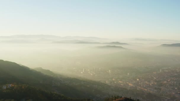 萨拉热窝的空中景观波斯尼亚和黑塞哥维那 无人机在西部飞行 日出在城市上空升起 房屋林立 街道被浓烟笼罩 山脉和山峰环绕着 — 图库视频影像