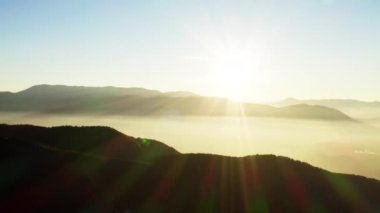Gün doğumunun havadan görünüşü, dağlarda gün batımı. Işıklı güneş, duman ve bulutlarla kaplı dağ sıralarını ve tepelerini aydınlatır. Güzel arkaplan manzarası videosu.