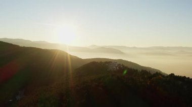 Gün doğumunun havadan görünüşü, dağlarda gün batımı. Işıklı güneş, duman ve bulutlarla kaplı dağ sıralarını ve tepelerini aydınlatır. Güzel arkaplan manzarası videosu.