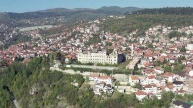 Aerial view Sarajevo Bosnia and Herzegovina. Drone video of an old historic palace which stands in the center of the city on a mountain surrounded by houses with red roofs and mountain ranges.