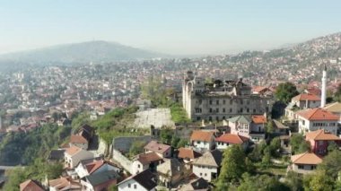 Aerial shot Bosnia and Herzegovina. Drone video of the cityscape of the European city of its central part with historic buildings, houses on the hills, river and mountains in the background.