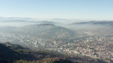 Saraybosna, Bosna-Hersek havadan görünüyor. İnsansız hava aracı dağların ve sıradağların üzerinden uçuyor. Tepeleri eteklerinde sokakları, şehir merkezleri ve evleri olan bir şehir var..