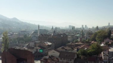 Aerial shot Sarajevo Bosnia and Herzegovina. Drone flying over the historic city center with old houses, streets, mosques and churches standing in the haze and in the background landscape mountains.