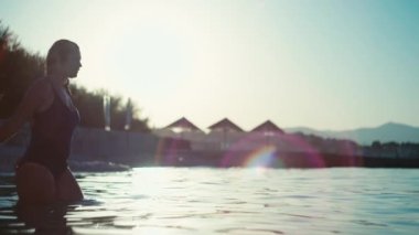 Denize atlayan ve yüzen bir kızın yavaş çekim videosu. Mayo giymiş güzel bir kadın dinlenirken okyanusa giriyor..