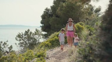 The family is walking on vacation by the ocean. Beautiful seascape and a woman with two children walk together on a path in the woods.