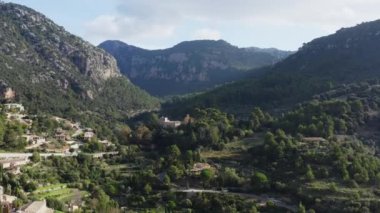 Ormanlarla kaplı dağ sıralarının havadan görünüşü. İnsansız hava aracı, kayalık dağların üzerinde uçurumlarla uçuyor. Ağaçlar, üzerinde evler olan yolun dibinde yetişiyor. Yüksek kalite 4k görüntü