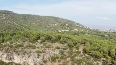 Dağ köyünün manzarası. Günbatımı dron 4K video. Dağ sıralarında, ağaçların tepeleri ve arka planda deniz olan ormanlar olan evler ve yolların havadan görünüşü. Yüksek kalite 4k görüntü