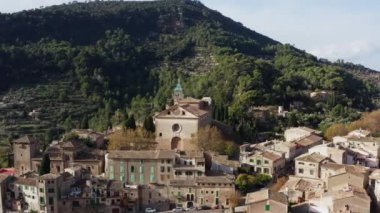 Mallorca İspanya dron 4K video adasındaki köy. Kilisenin eski sokaklarının evleri ile köyün havadan görünüşü. Dağlar ve kayalarla kaplı bir arazide duruyor..