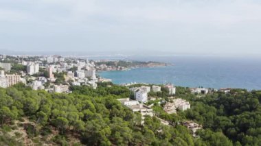 Akdeniz dron 4K videosundaki dağlardaki şehir. Gökyüzü manzaralı evler ve sokaklar, deniz dalgalarının çarptığı çam ağaçları ile dağların zirvelerinde duruyor. Yüksek kalite 4k görüntü