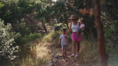 Woman with two children on a walk in the park. Beautiful young mother carries her daughter in her arms and holds her sons hand.