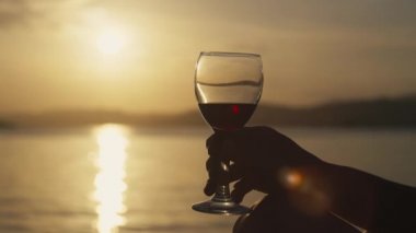 Gün batımında deniz manzarasında cam tutan kadın elleri. Okyanus kıyısında romantik bir buluşma güzel bir manzarada bir bardak şarabın yakın çekimi.