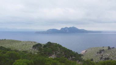 Akdeniz dron 4K videosunun yakınlarındaki sıradağlar. Üzerinde ağaçlar ve ormanlar yetişen kayalar ve uçurumlarla dolu dağların tepeleri denizin dalgalarıyla yıkanır.. 