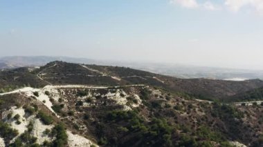 Kıbrıs havadan görünüyor. İnsansız hava aracı uçuşu dağların, tepelerin ve kayaların üzerinde ağaçlar ve çalıların yetiştiği ve yolların uzadığı güzel bir arazide gerçekleşir. Yüksek kalite 4k görüntü