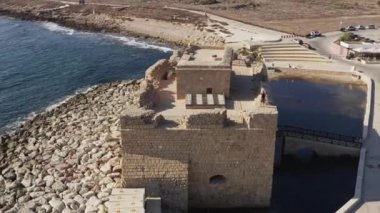 Drone flying over the old historic fort that stands on the shores of the Mediterranean Sea against the shoreline of which the waves crash. Aerial view Paphos Cyprus. High quality 4k footage