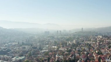 Aerial shot Bosnia and Herzegovina. Drone video of the cityscape of the European city of its central part with historic buildings, houses on the hills, river and mountains in the background.