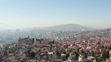 Drone flying over the old quarter of the city with houses with red roofs, churches, mosques and a beautiful mountain landscape. Aerial view Sarajevo Bosnia and Herzegovina.