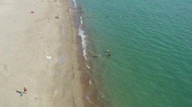 Güneşlenen ve yüzen insanların ve Akdeniz 'in dalgalarının kıyıları yıkadığı kumlu bir şehir plajının insansız hava aracı videosu. Antalya Türkiye 'nin deniz manzarası. Yüksek kalite 4k görüntü