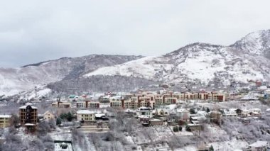 Kışın şehrin insansız hava aracı görüntüsü. Şehir merkezinde çatıları olan evler ve caddeler karla kaplı, dağlar ve zirveler arasında duruyor. Hava manzaralı Almaty Kazakistan. Yüksek kalite 4k 