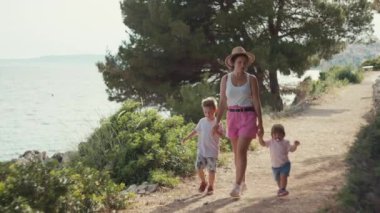Çocuklu bir aile deniz kenarında parkta yürüyüşe çıktı. Mutlu çocuklar ve anne yolda yürüyor ve gülümsüyor..