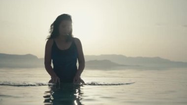 Girl standing in the ocean water at sunset. Fashion slow motion video of a beautiful Caucasian woman in a swimsuit relaxing in the sea on vacation.