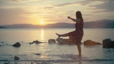 Girl splashes water with her feet in the sea at sunset. Happy and smiling Caucasian woman dancing in the ocean.