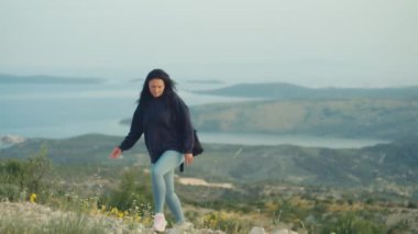 Slow motion video of a woman with a backpack climbed to the top of the mountain. Beautiful landscape of mountains and sea and a happy girl who has conquered the mountain.