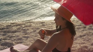 Kadın vücuduna güneş kremi sürüyor. Kumsalda dinlenen güzel bir kızın yavaş çekim videosu..