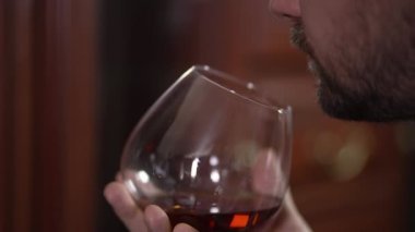 Bir adamın elinde bir bardak konyak adamı kokluyor. Ev brendisinde alkollü içecek. Alkollü bir adamın 4K 'lık güzel videosu. Yüksek kalite 4k görüntü