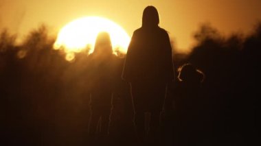 Family walks in a beautiful landscape at sunset. Silhouette of a mother with two daughters walking on a path in the park. Slow motion 4K video of a happy family. High quality 4k footage