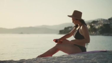 Kız, okyanus kıyısındaki plajda cesede güneş kremi sürüyor. Güzel beyaz kadın tatilde güneşleniyor..