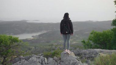 The girl conquers the top of the mountain and raises her hands to the top. Beautiful woman with a backpack hiking in the mountains, victory, feeling of freedom alone with the mountains.
