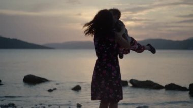 Anne ve oğlu gün batımında deniz kenarında sevinçten havalara uçuyor. Tatilde mutlu bir aile okyanus kenarında dans ediyor..