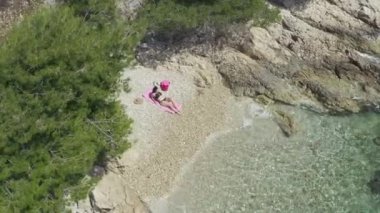 Deniz kenarında mayo giymiş havadan bakan kız. Okyanusun dalgaları bir kadının dinlenip dinlendiği sahili yıkıyor..