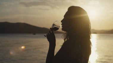 Gün batımında deniz kenarında şarap içen bir kız. Okyanusun kenarında bir bardak şarabı olan kadın dinleniyor ve dinleniyor..