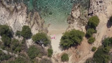 Aerial view girl in swimsuit sunbathing alone on the beach by the sea. Beautiful landscape and woman lying on rocks in the sun by the ocean on vacation and relaxing.