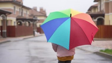 Renkli şemsiyeli bir kız caddede yürüyor. Evleri ve çiçek tarhları olan güzel bir yer. Yağmurlu havalarda çocuk oraya gider..