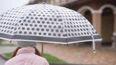 Çocuk yağmurda elinde bir şemsiyeyle caddede yürür. Kız, üzerine yağmur damlalarının düştüğü bir şemsiyeyi çevirir..