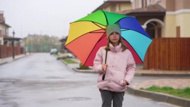 Portrait of a girl with an umbrella in the cityscape. A child in a hat jacket jeans and sneakers stands on the street in a new neighborhood with beautiful architecture.