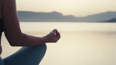 Güneş doğarken okyanus kenarında meditasyon yapan bir kadının ellerine yakın çekim. Denizde yoga yapan kız..