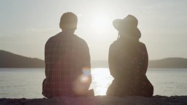 A man and a woman are sitting at sunset by the sea. Romantic atmosphere and people in love hugging by the ocean. High quality 4k footage